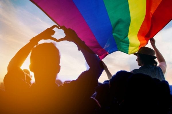 Pride community at a parade with hands raised and the LGBTQ flag